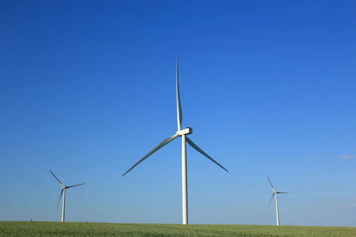 Wind turbines generating electricity above green fields